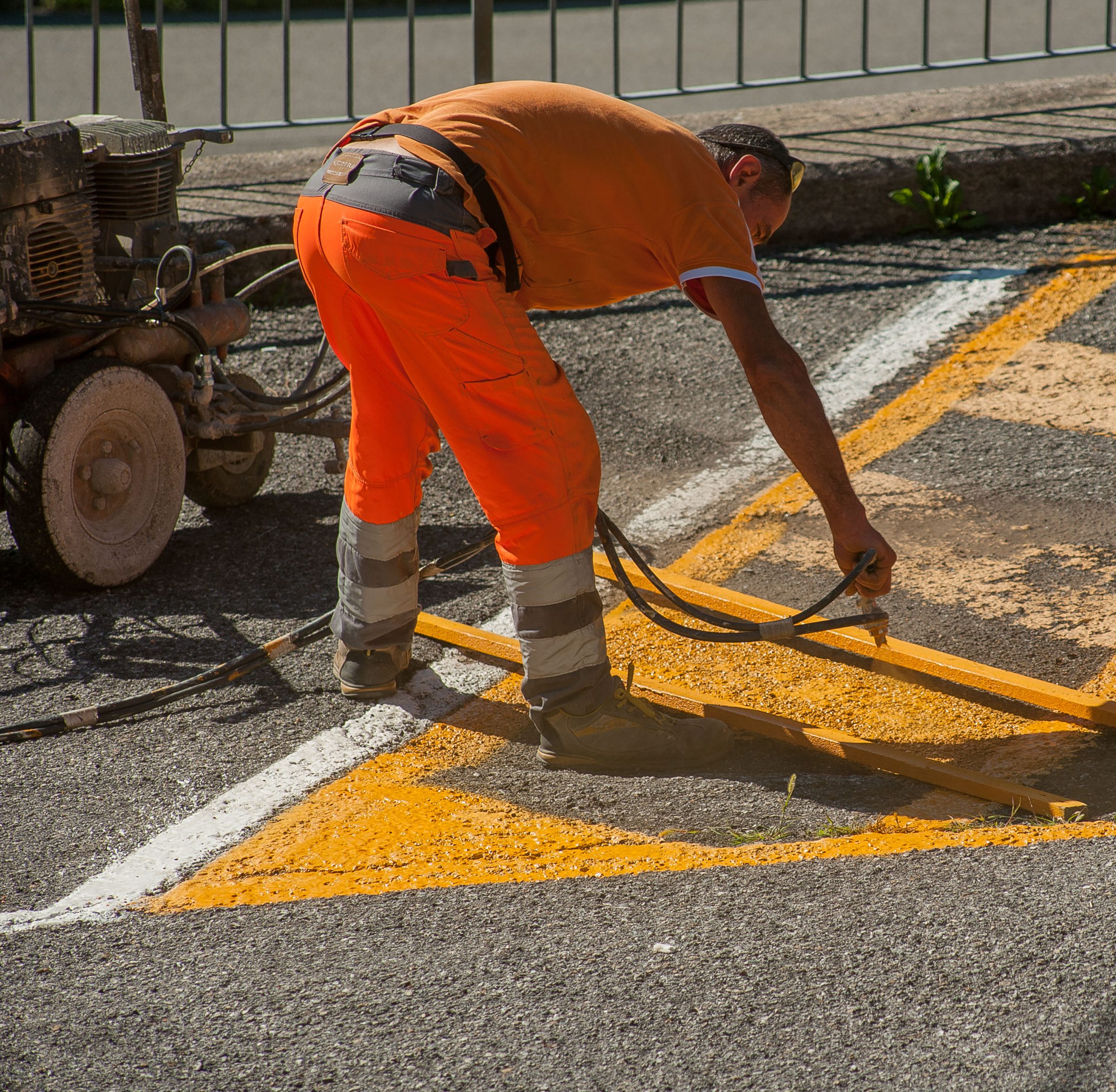 Ouvrier en tenue orange peignant un marquage jaune au sol